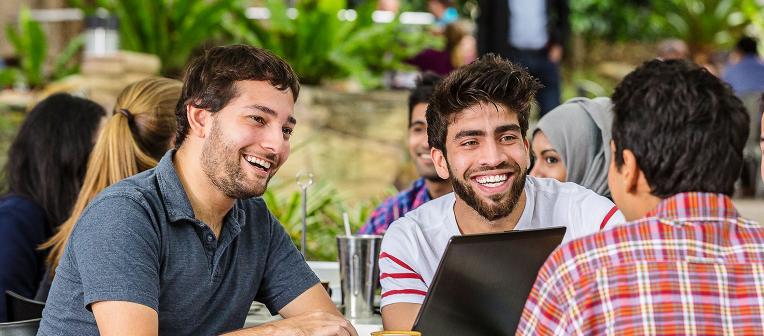 Three men talk over a laptop outdoors. 