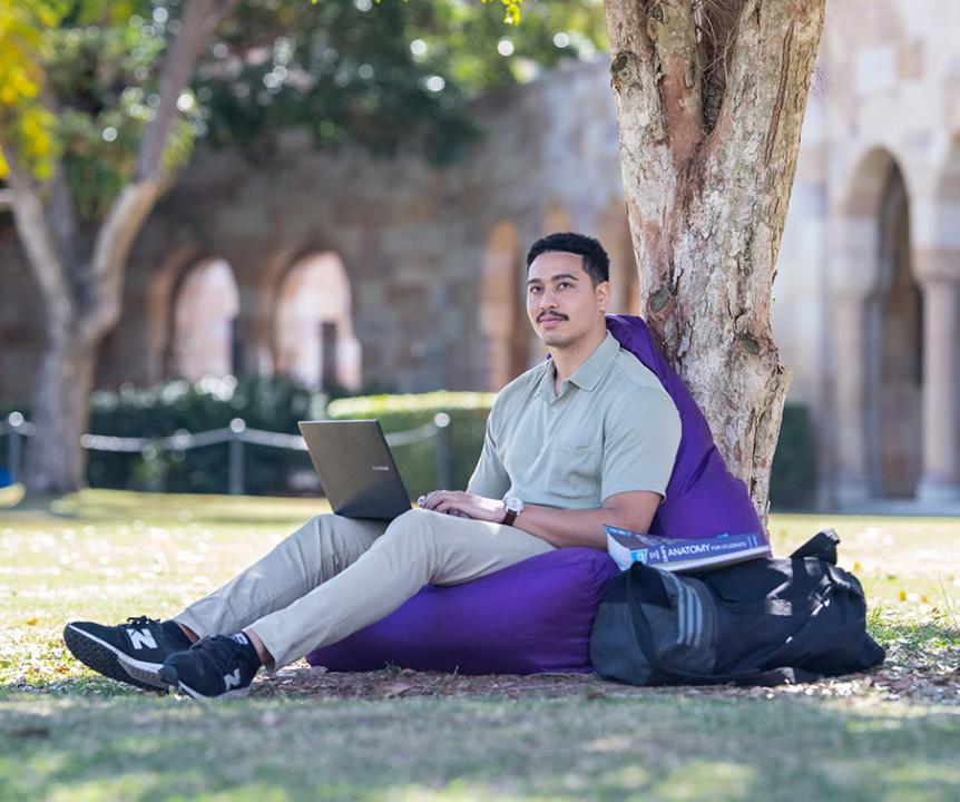 Student at St Lucia campus leaning against tree